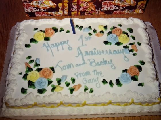 A cake reading "Happy 1st Anniversary Tom and Becky, From the Gang"